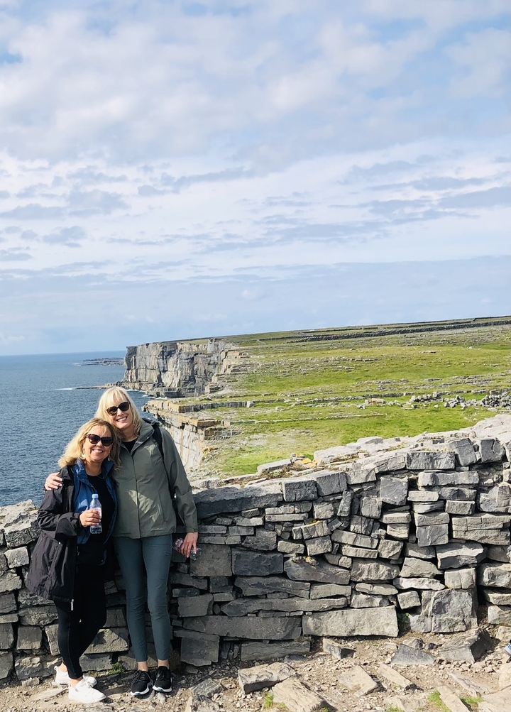 Two women posing at a coastal landscape with cliffs.