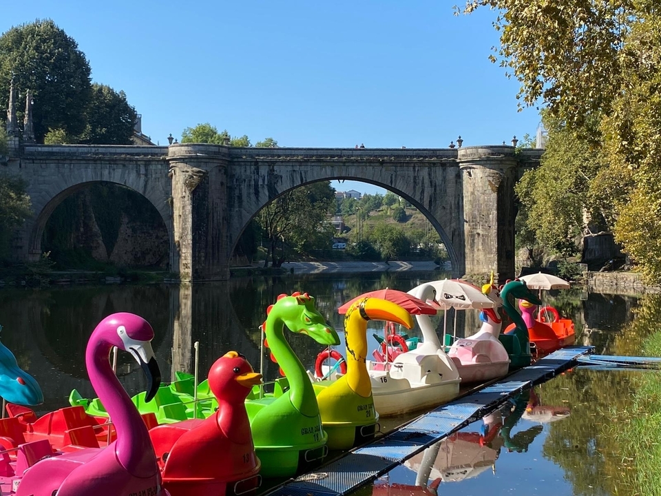 Pédalos colorés sur une rivière avec un pont historique.