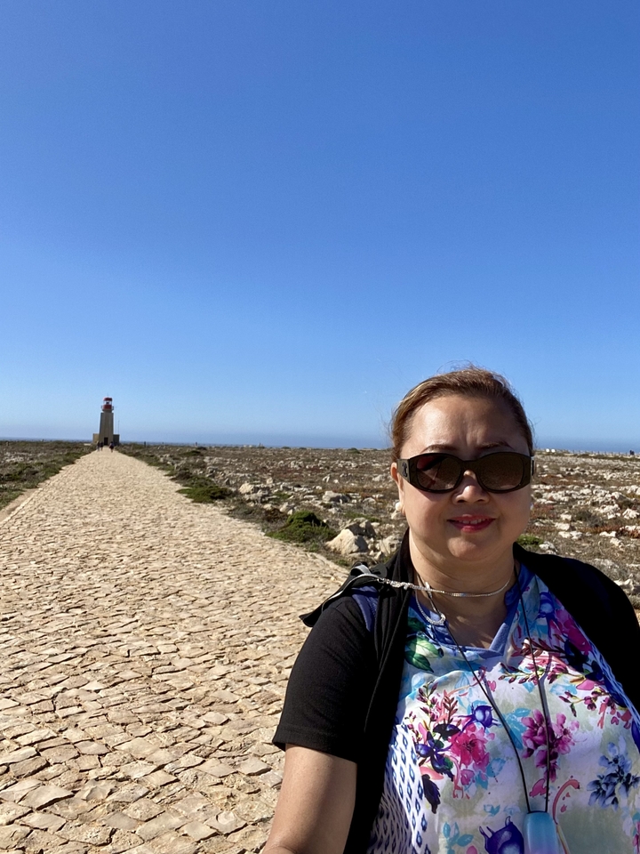 Woman with sunglasses at a coastal area with a lighthouse.