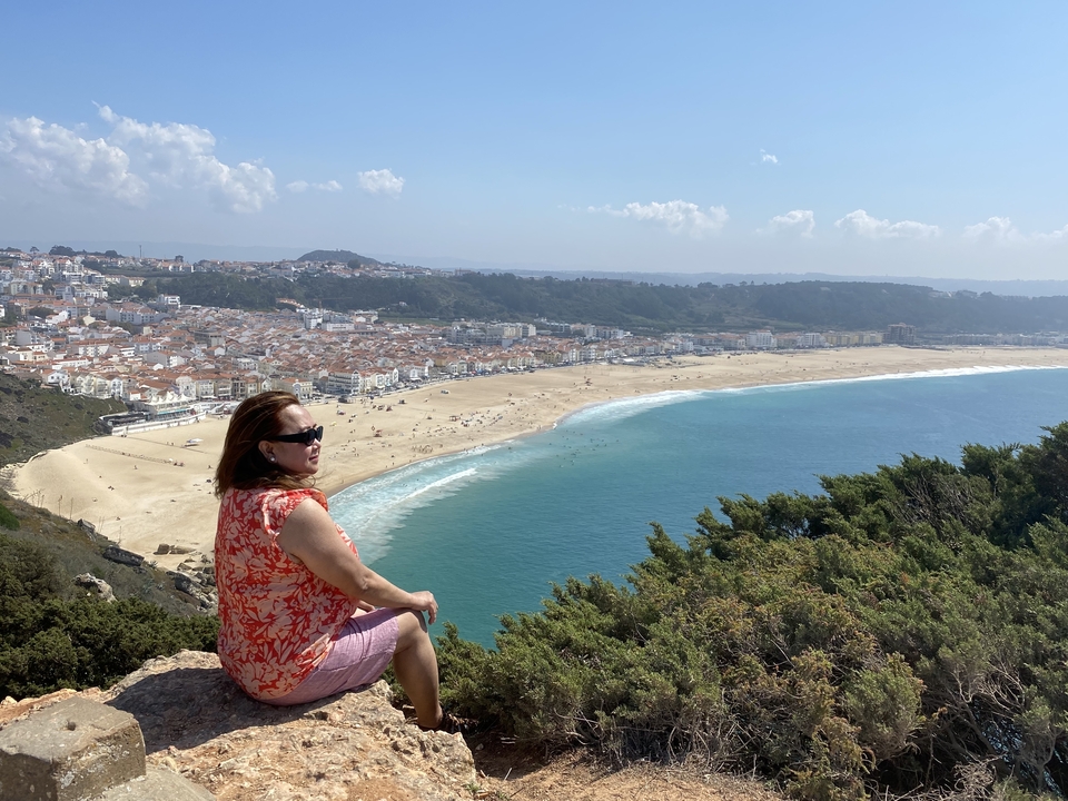 Woman sitting on a cliff overlooking a large beach in a city.