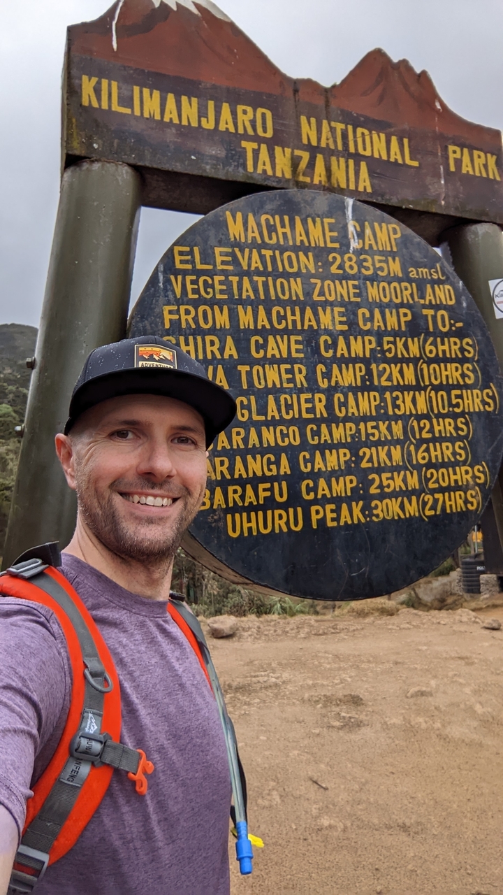 Man standing next to a sign displaying different camp routes.