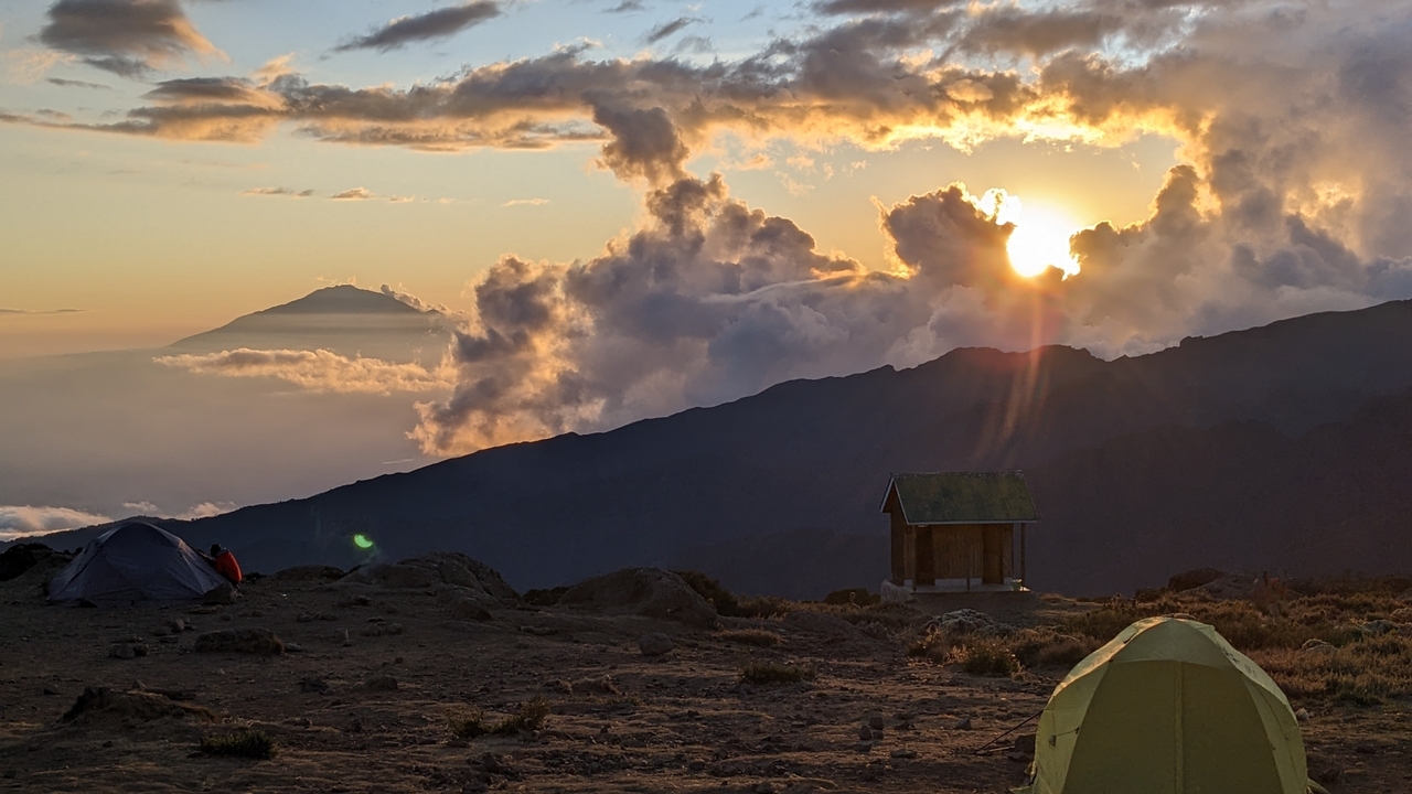 Sunrise view over mountains with tents on the foreground.