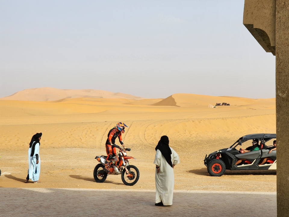 Motorcyclist in desert area with people and a dune buggy.
