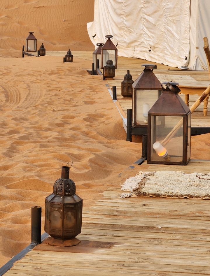 Close-up of lanterns and rug on sand.