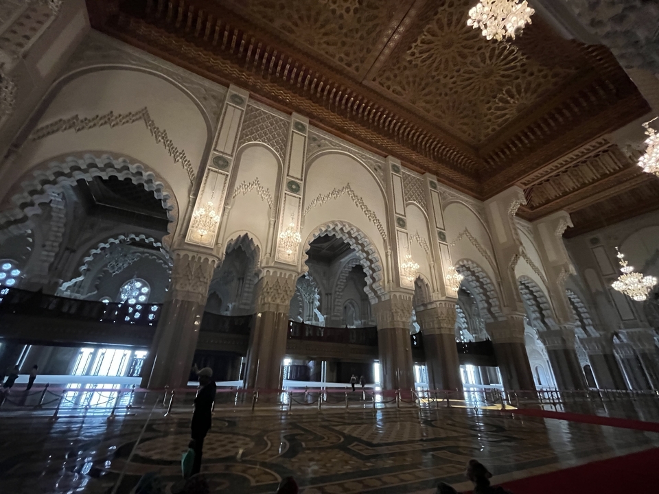 Interior of a grand mosque with intricately decorated arches and chandeliers.