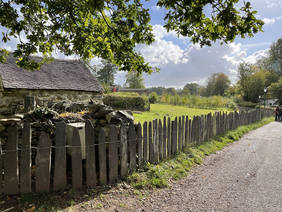 Countryside path with stone buildings and a fence.