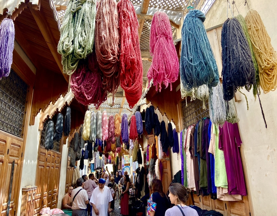 Market scene with colorful textiles hanging above.