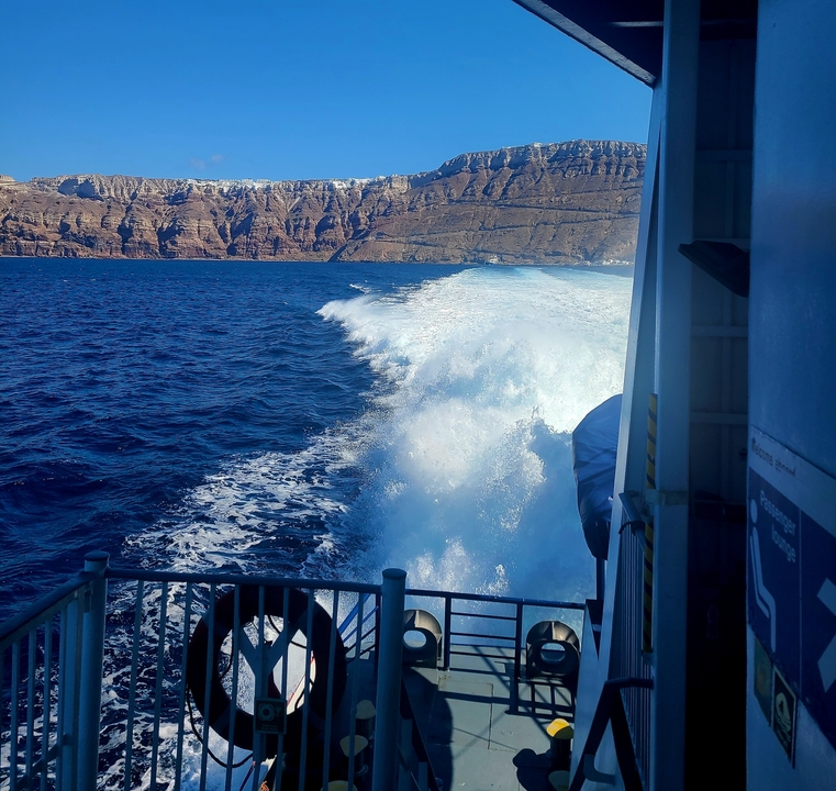 View from a boat with waves and rocky cliffs in the distance.