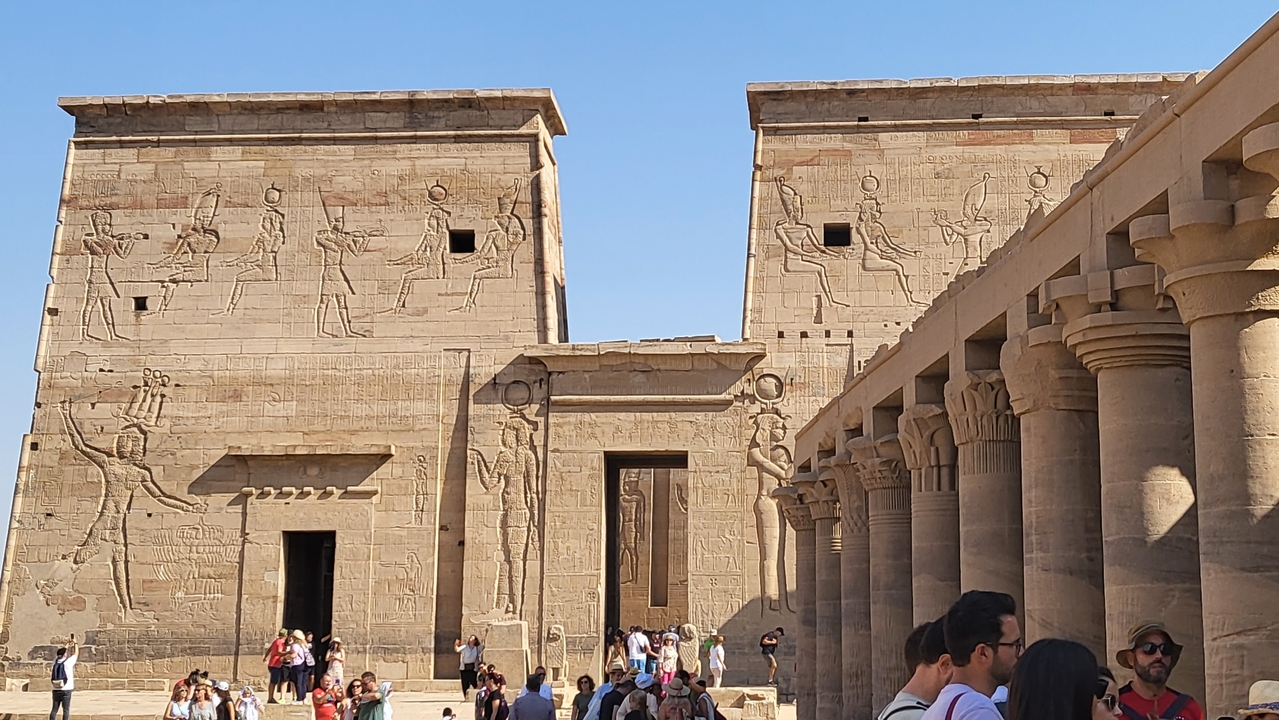 Temple ruins with columns and wall carvings, with people visiting.