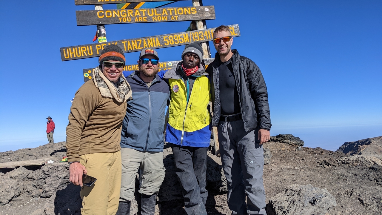 Four people posing at Uhuru Peak with a sign.