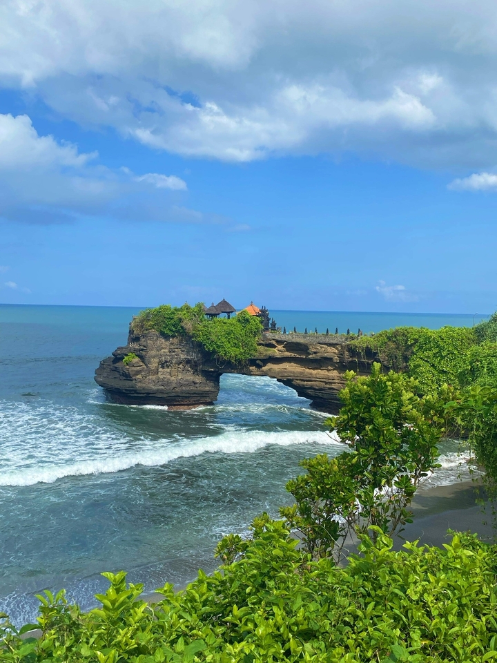 A natural rock arch over the sea with lush greenery.