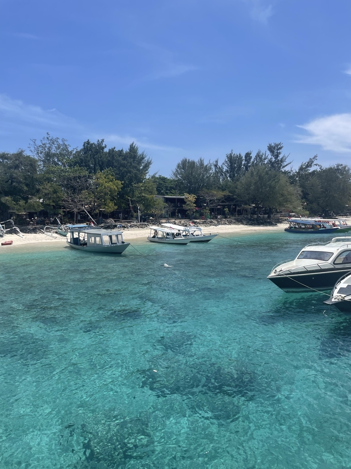 Clear turquoise waters with boats moored along a sandy beach.