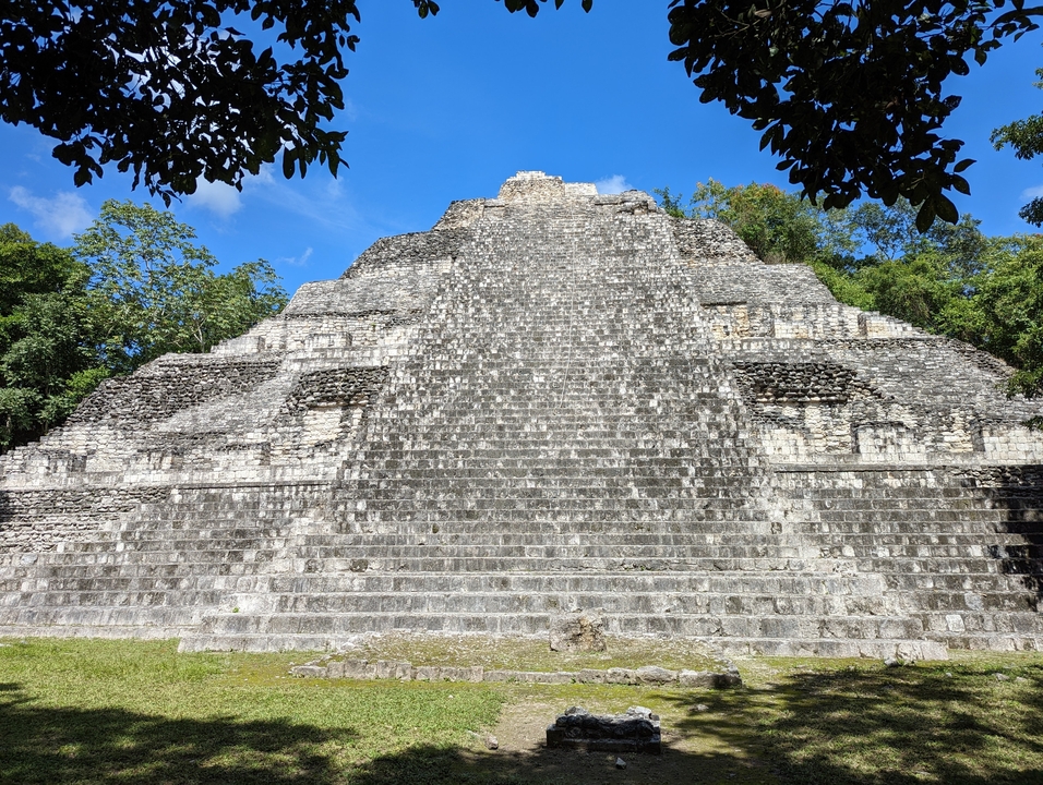Large stone pyramid in a forest with clear blue sky.