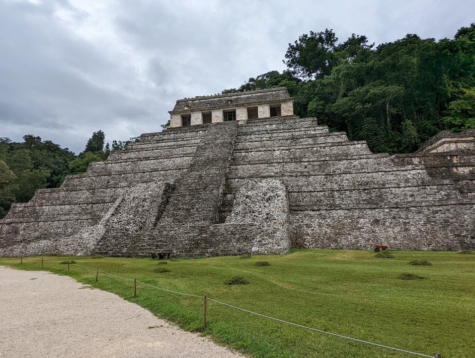 Stone pyramid with grass steps surrounded by forest.