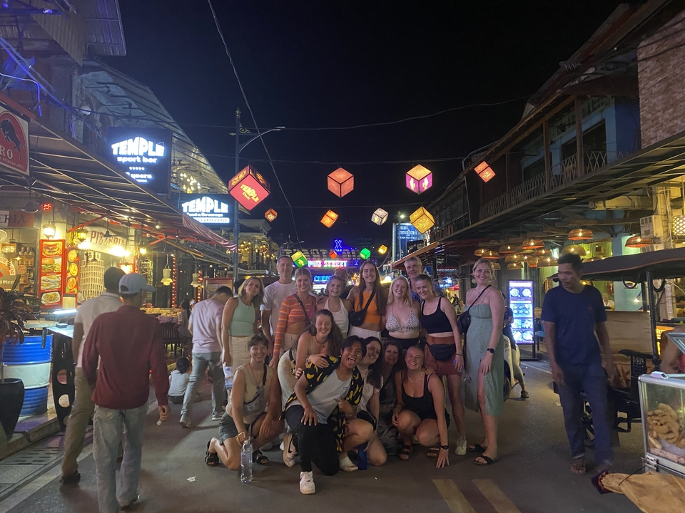 A group of people posing under colorful lanterns in a busy street at night.