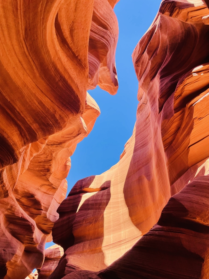 Canyon with smooth red curves and a bright blue sky visible above.