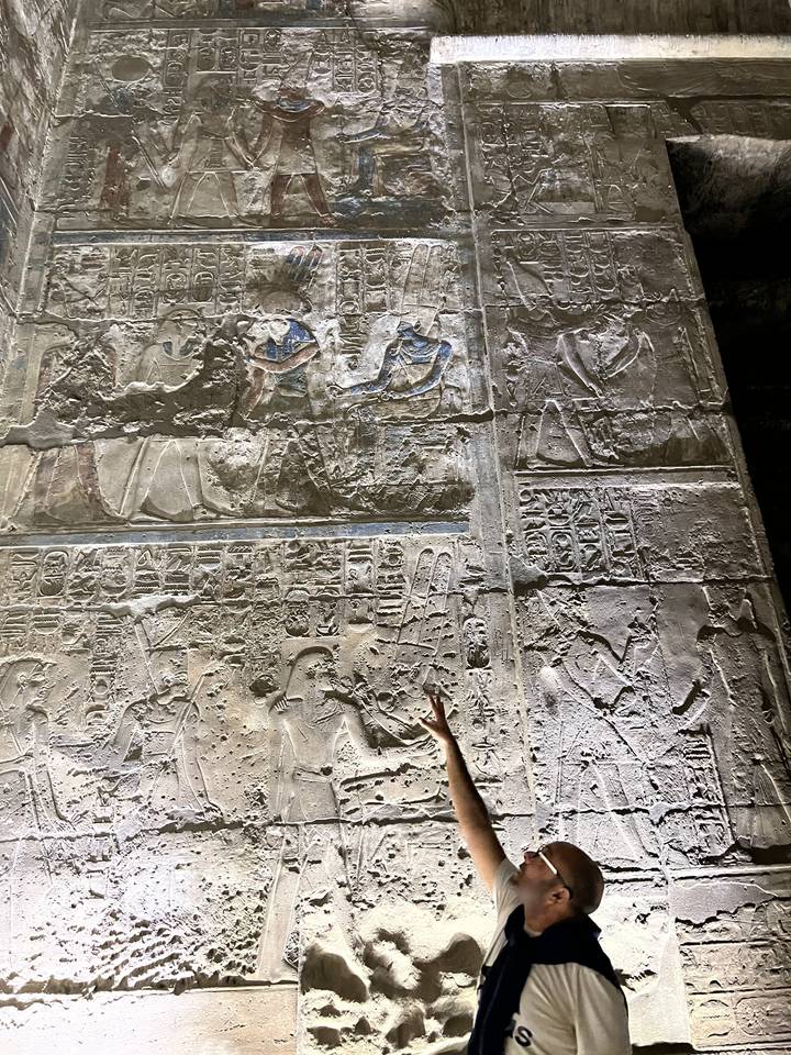 A person pointing at ancient Egyptian reliefs on a wall.