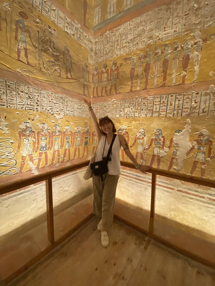 Person with arms outstretched in an ancient tomb with hieroglyphics.