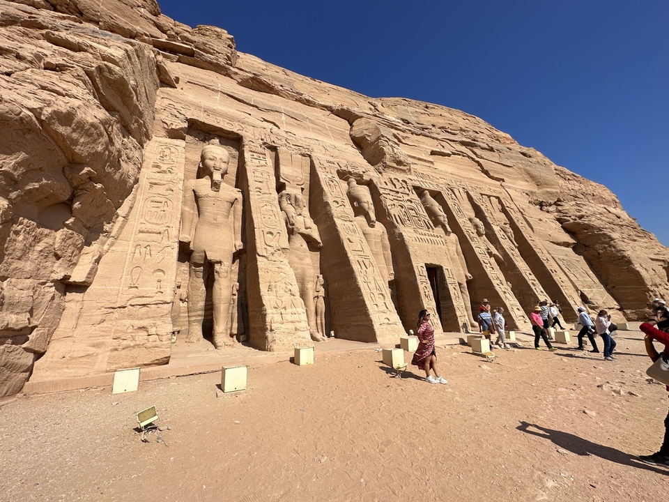 Tourists walking around Abu Simbel temple with large statues and hieroglyphs.