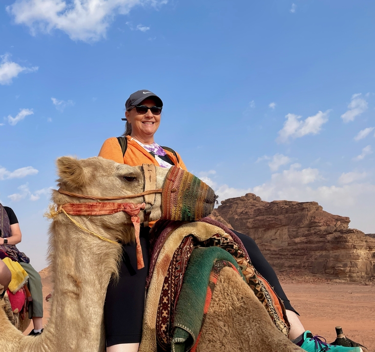 Woman riding a camel in a desert landscape.