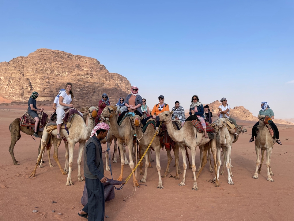 Group of people riding camels in a desert setting.