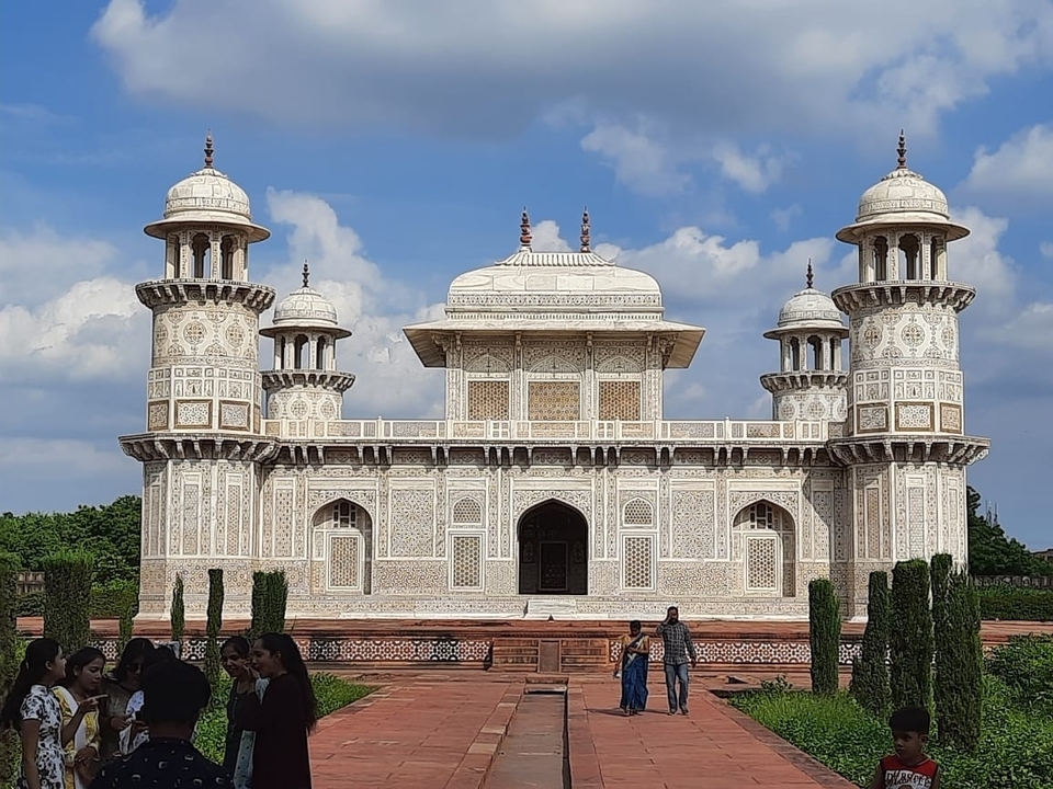 White marble mausoleum with intricate decorations and people.