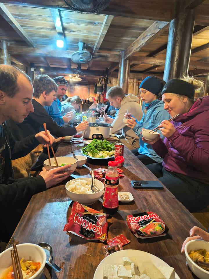 Group of people sitting at a wooden table sharing food.
