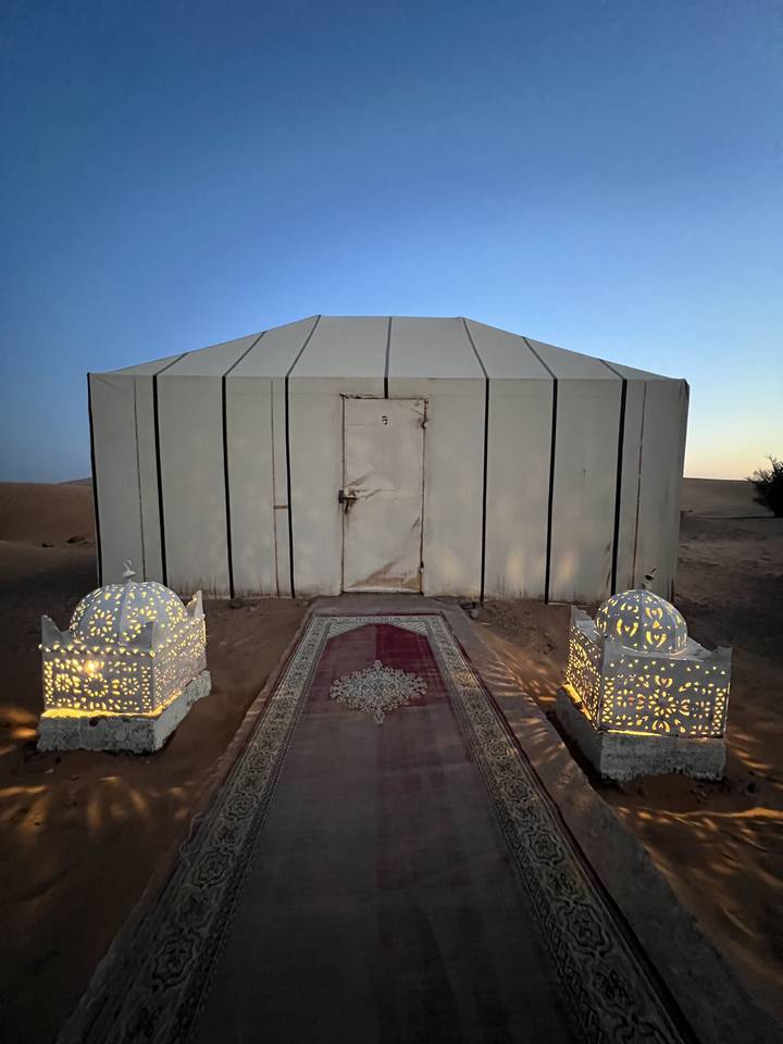 A desert camp setup with ornate lamps and a pathway leading to a tent.