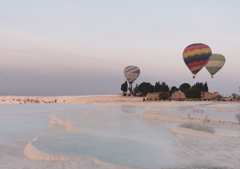Hot air balloons over white terraces at sunset.