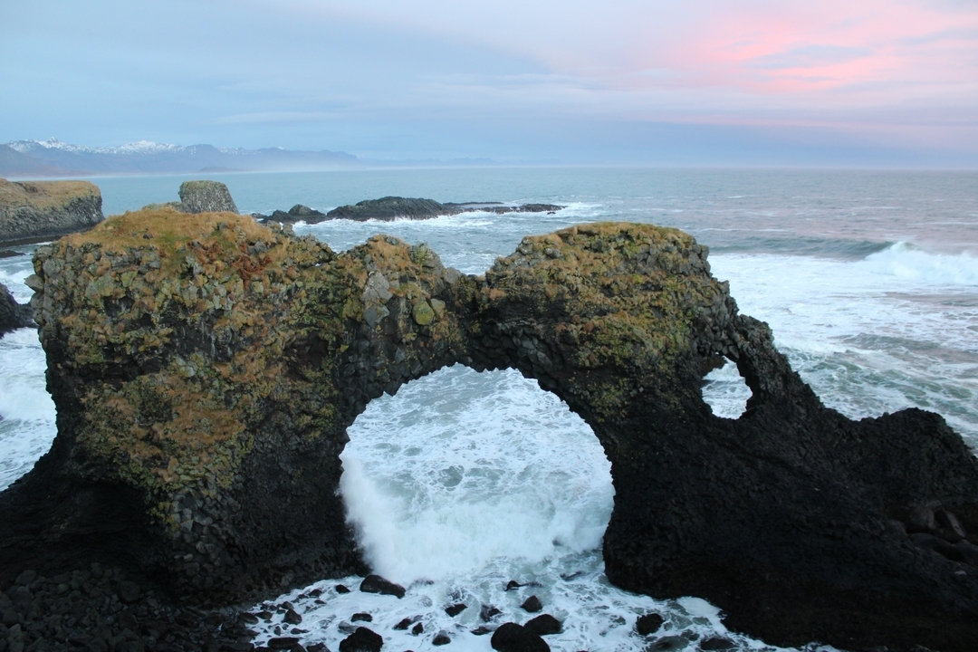 A natural stone arch by the ocean with waves crashing.