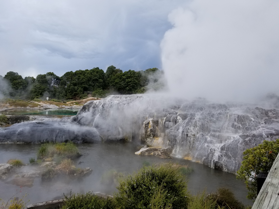 Geothermal area with steam rising from rocky formations.