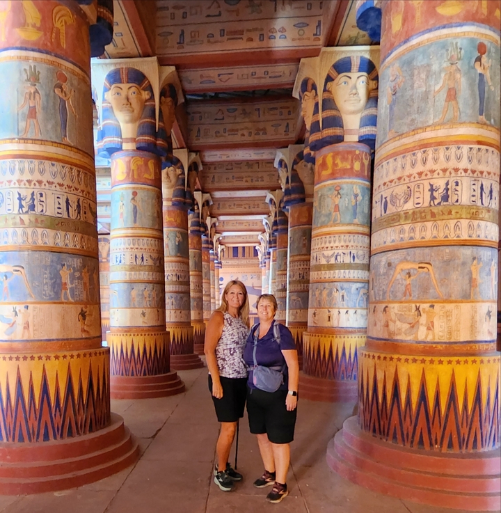 Two people standing inside a hall with ornately painted columns.