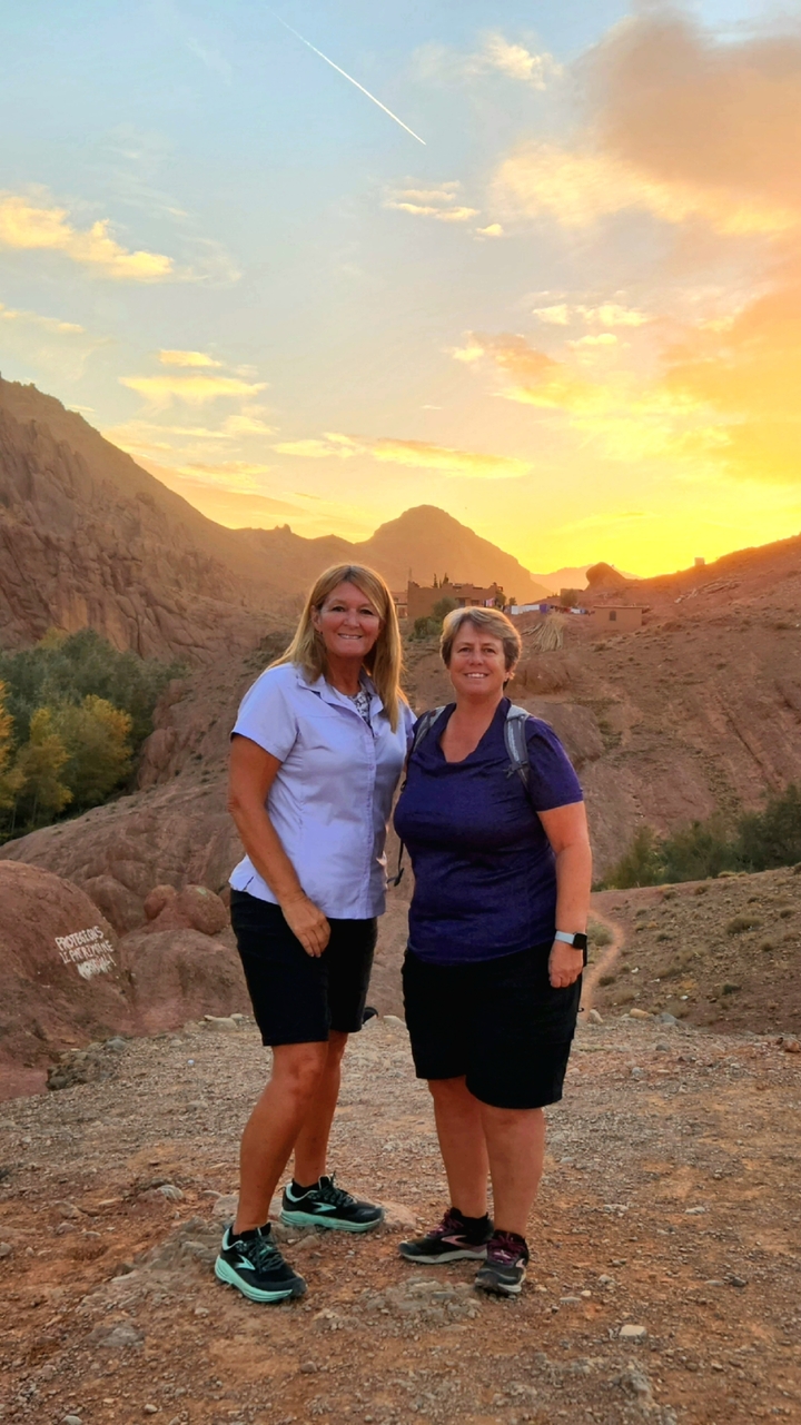 Two people posing with a scenic view of the desert mountains at sunrise.