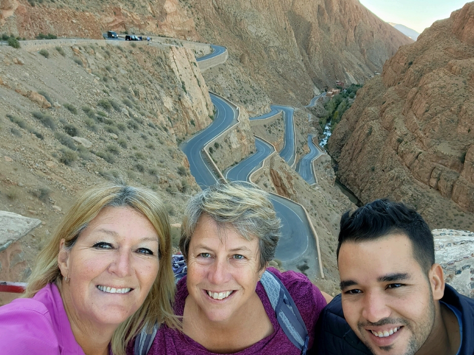 Three people taking a selfie with a view of winding canyon roads.