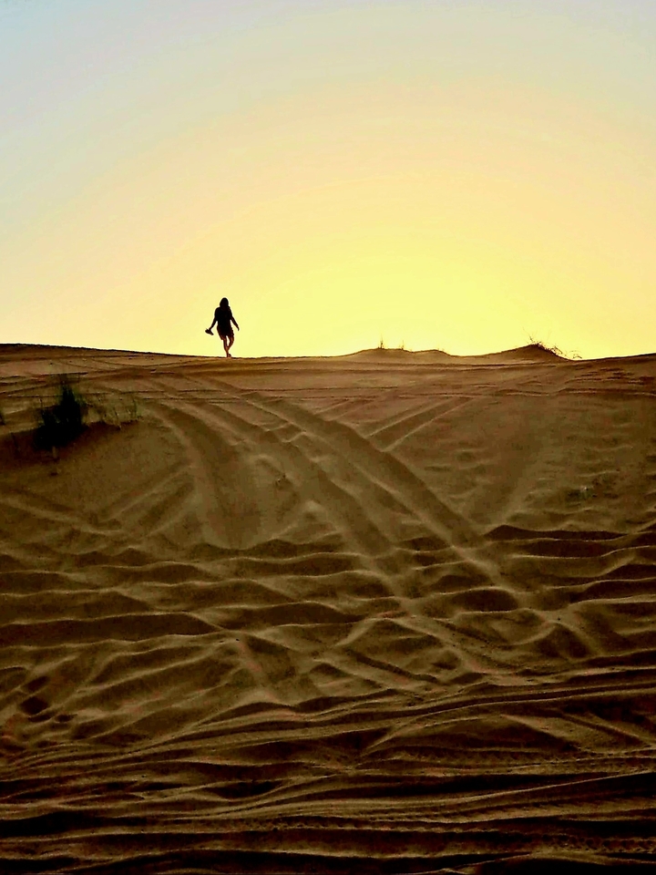 Person walking on sand dunes at sunset.