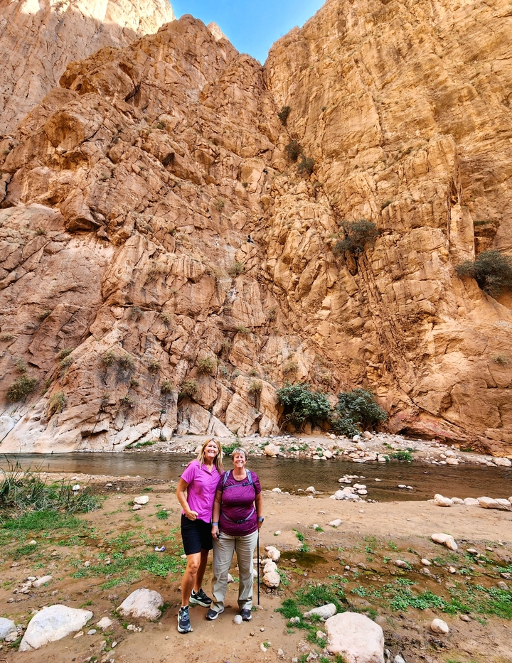 Two people smiling in front of a large rock formation with a river.