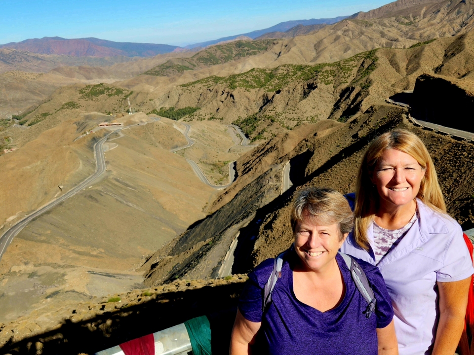 Two people posing with a winding mountain road in the background.