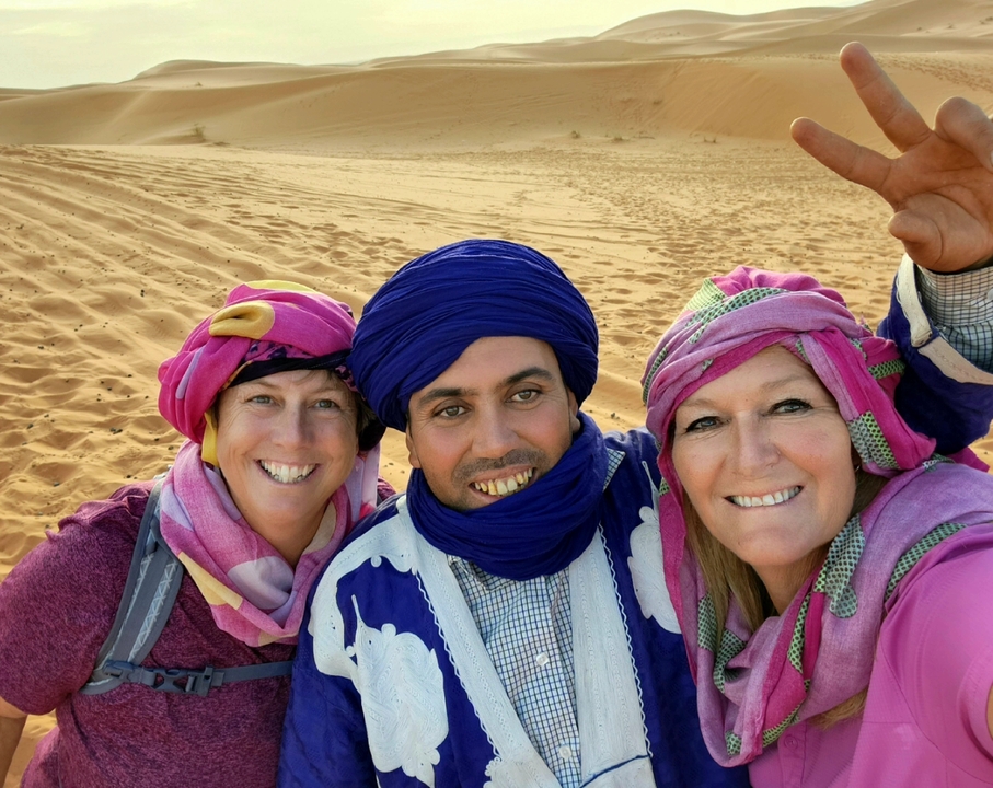 Three people wearing traditional attire in a desert setting.