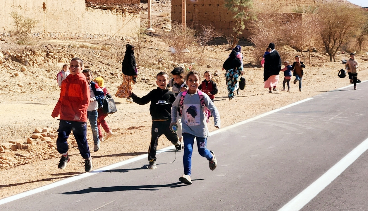 Children walking and running along a road in a rural desert area.