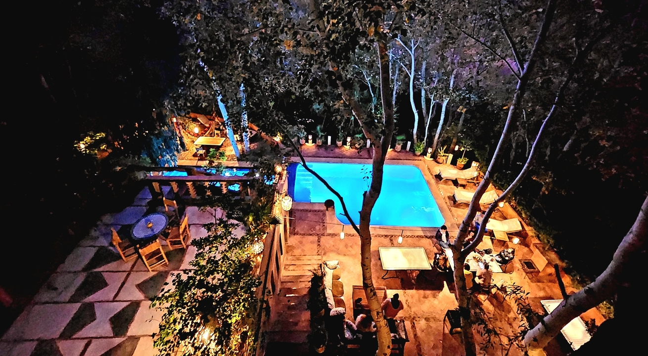 Night view of a beautifully lit outdoor pool area surrounded by trees and seating.