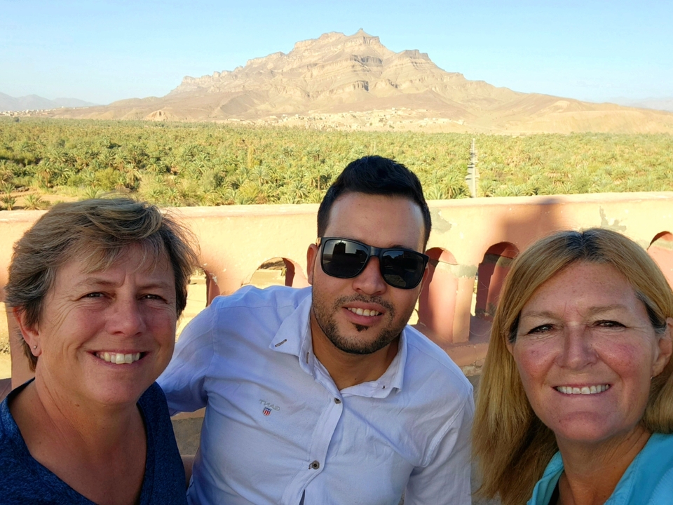 Three people posing with a palm grove and mountains in the background.