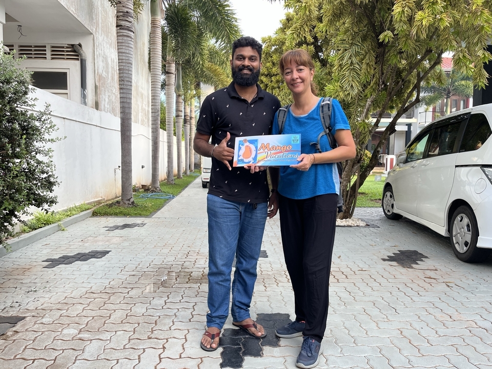Two people posing with a brightly colored 'Mango Madness' sign.
