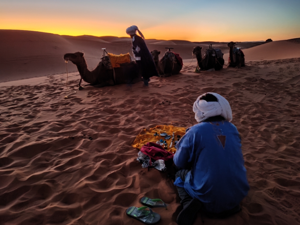 Des personnes avec des chameaux dans un paysage désertique au coucher du soleil.