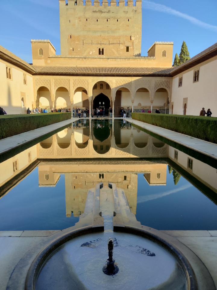 Reflet d'un bâtiment historique dans un bassin avec des gens autour.