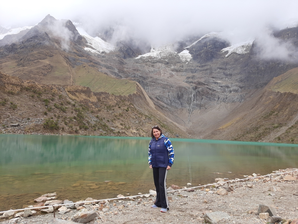 Woman posing by a turquoise glacial lake with a snowcap in the background.