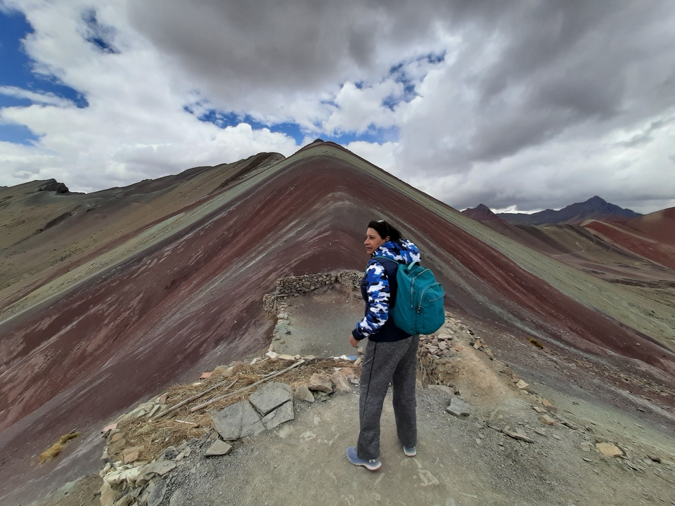 Hiker standing on a path with the colorful Rainbow Mountain behind.