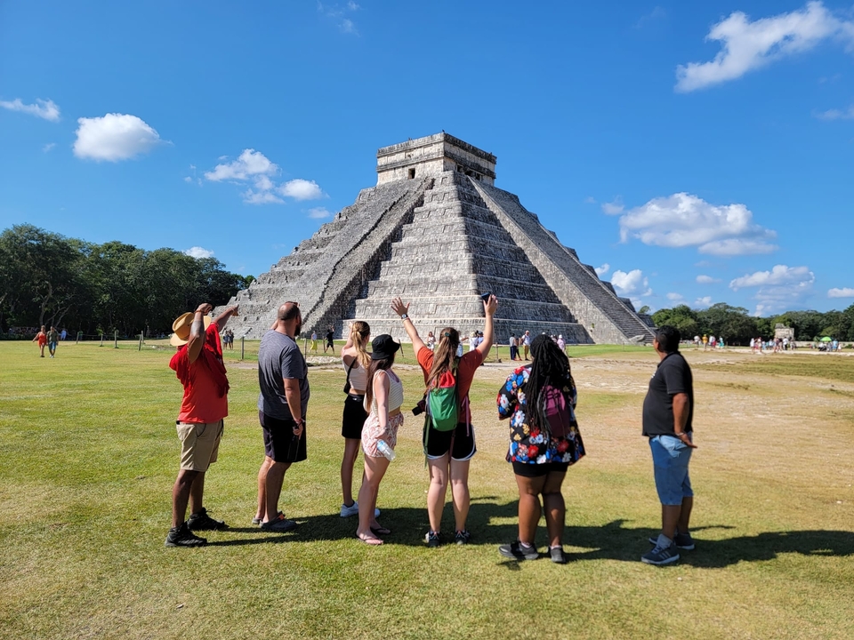 A group of people posing in front of a stone pyramid.
