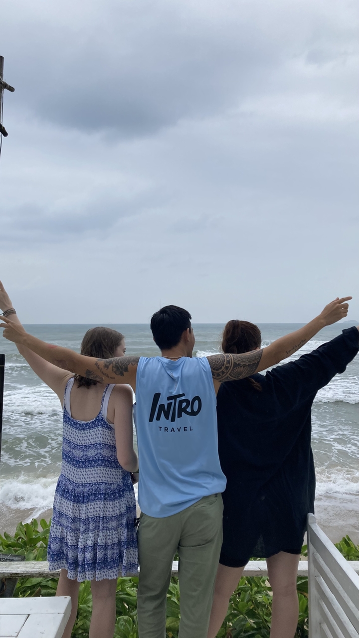 Three people standing with their arms up, facing the ocean.