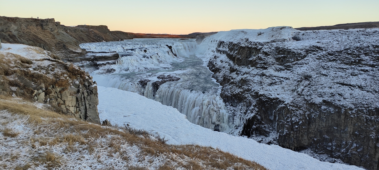 Frozen waterfall surrounded by snow-covered cliffs.