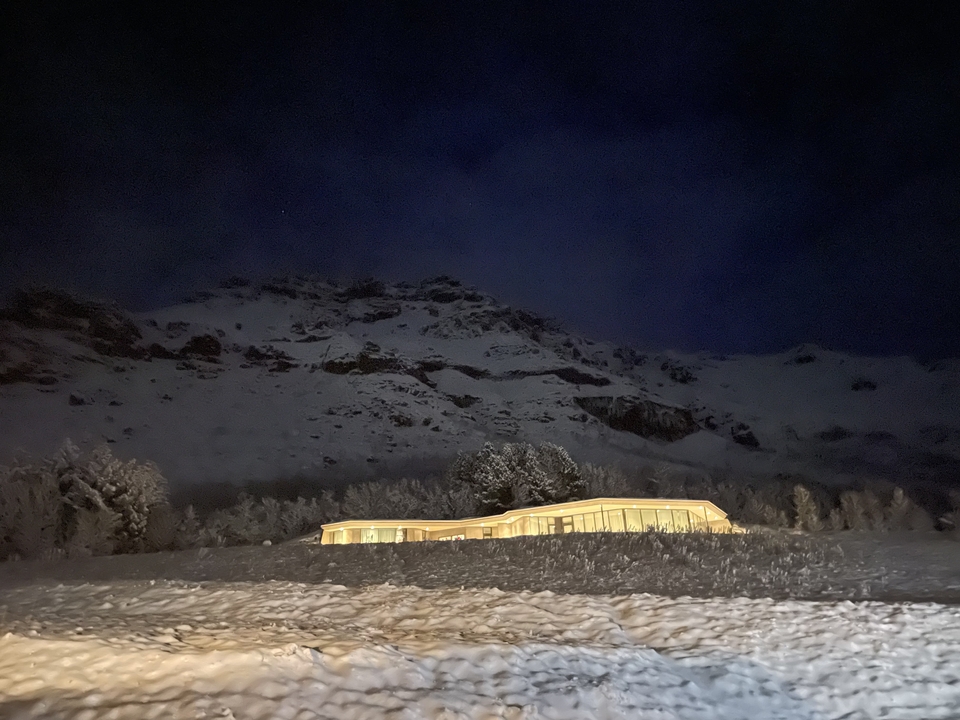 A lit modern building in a snowy landscape at night.